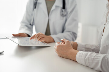 Doctor and patient discussing current health examination while sitting at the desk in clinic office. The focus is on female patient's hands, close up. Perfect medical service and medicine concept.