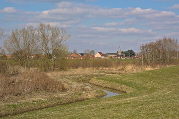 Creek along meadow with bare winter trees and golden reed and houses and church in the background...