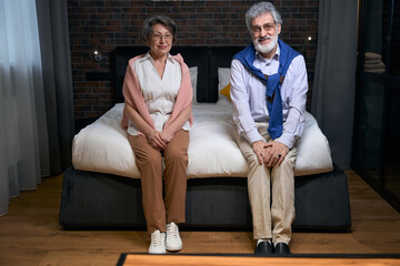 Satisfied mature married couple settled down on a large bed