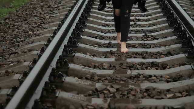 A girl walks barefoot on a railroad track. Dramatic background of suicidal thoughts. Desperate woman wants to commit suicide on the railroad. Young girl with psychological or mental problems.