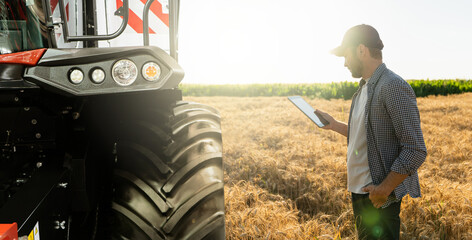 Farmer with digital tablet stands next to combine harvester. Smart farming concept.	