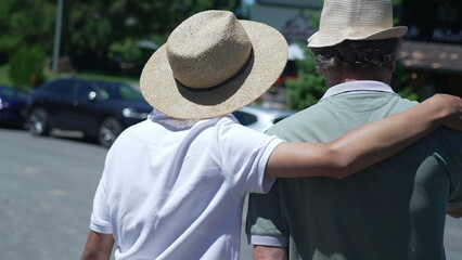 Back of son embracing father with arm around walking outside together wearing Panama Hats during sunny beautiful day