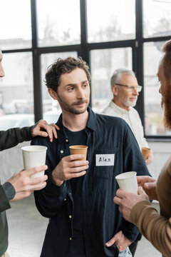 People with paper cups talking to man during alcoholics meeting in rehab center.