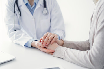 Doctor and patient sitting at the table in clinic office. The focus is on female physician's hands...