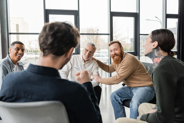Cheerful interracial group of people with alcohol addiction talking in rehab center.