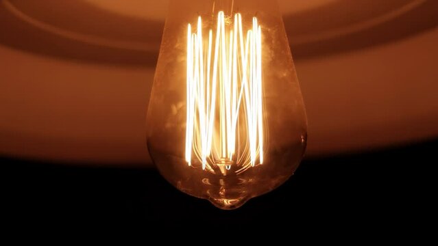 L&acirc;mpada de filamento de carbono emitindo luz amarela por dentro do abajur e girando devagar
