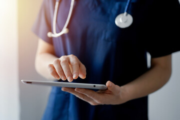 Doctor woman using tablet computer while standing near panorama window in clinic, close up. Physician or surgeon at work. Medicine concept.