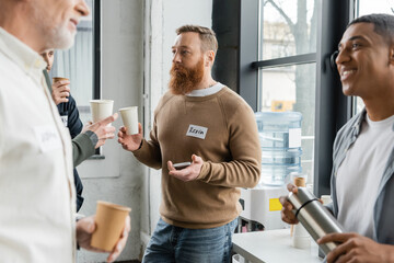 Obraz premium Bearded man with paper cup and smartphone talking to people during alcoholics meeting in recovery center.