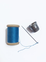 A spool of blue thread, thimble and needle