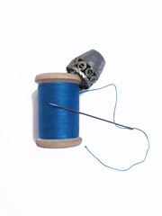 A spool of blue thread, thimble and needle