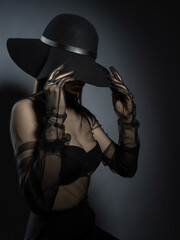 Fototapeta na wymiar Fashion portrait of a young girl in a black bra and transparent top. Felt black hat. Model posing, faces not visible photo in studio.