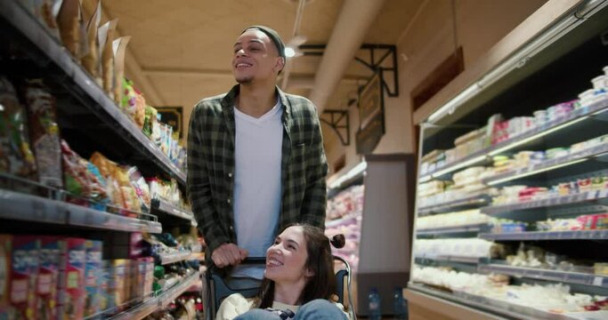 Young couple having fun, man pushing shopping cart with his girlfriend inside