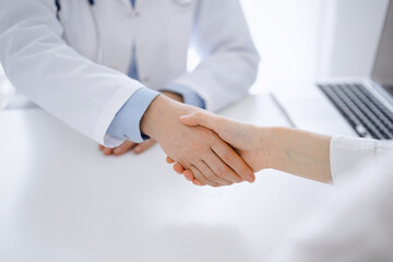 Obraz premium Doctor and patient shaking hands while sitting opposite of each other at the table in clinic, just hands close up. Medicine concept.