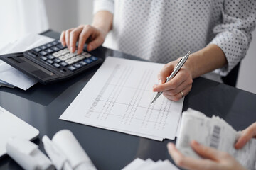 Woman accountant using a calculator and laptop computer while counting taxes for a client. Business audit and finance concepts.