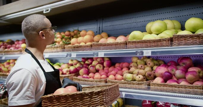 Worker in black apron arranging fresh citrus in supermarket section