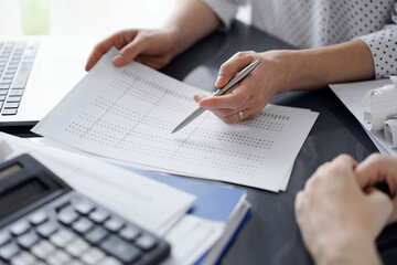 Female accountant pointing with a pen into audit paper while explaining tax counting results, close up. Business audit and finance concepts.