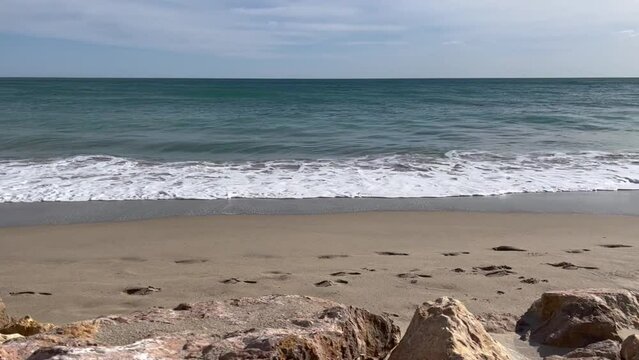 Olas rompiendo en la playa, con rocas en primer t&eacute;rmino