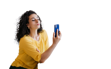Young adult curly woman in yellow blouse holds phone makes video call, selfie against transparent background. Hispanic housewife reads message on smartphone. Mockup, chatting female.