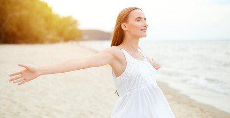 Happy smiling woman in free happiness bliss on ocean beach standing with open hands. Portrait of a multicultural female model in white summer dress enjoying nature during travel holidays vacation