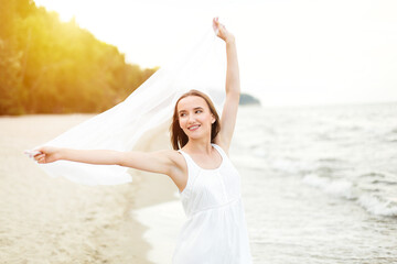 Fototapeta na wymiar Happy smiling woman in free happiness bliss on ocean beach standing with open hands. Portrait of a multicultural female model in white summer dress enjoying nature during travel holidays vacation