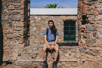 Young Latin man with long hair looking at camera sitting on a cobblestone wall.