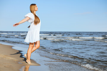 Fototapeta na wymiar Happy smiling beautiful woman is walking on the ocean beach with open arms.