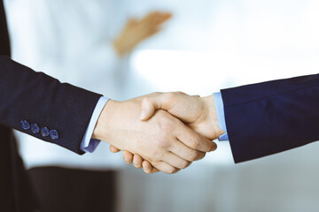 Business people shaking hands at meeting or negotiation, close-up. Group of unknown businessmen and a woman standing in a modern office. Teamwork, partnership and handshake concept.