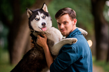Fototapeta premium Portrait of a handsome young man and his pet dog Siberian Husky in nature.