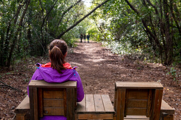 A woman sitting on a bench with her back turned in Gunnucek Milli Parki. Green oriental sweetgum...