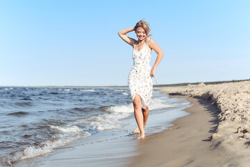 Fototapeta na wymiar Happy blonde beautiful woman having fun on ocean beach while dancing in waves.