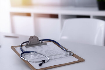 Stethoscope and clipboard with medication history records are on the table at sunny doctor's working place. Medicine concept