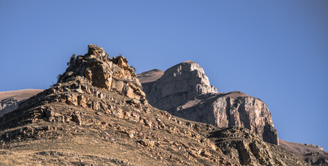 Rock formations protrude from a mountain and grassy hills on a sunny autumn morning