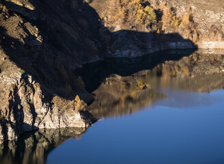 Rocky shore on the lake and reflection in the water in autumn at dawn, cliff break above the water