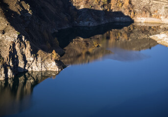 Rocky shore on the lake and reflection in the water in autumn at dawn, cliff break above the water