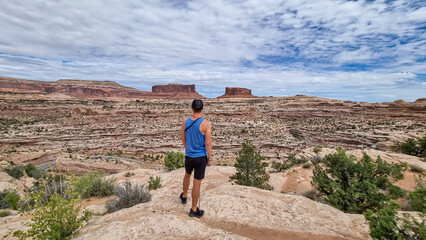 Fototapeta premium Man with panoramic view on Monitor and Merriamac Rock Formations near Moab, Canyonlands National Park, San Juan County, Utah, USA. Looking at natural pothole rock formation near Island in the Sky Mesa