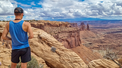 Fototapeta premium Man with panoramic view on Buck Canyon seen from Mesa Arch near Moab, Canyonlands National Park, San Juan County, Utah, USA. Looking at natural pothole arch rock formation near Island in the Sky Mesa