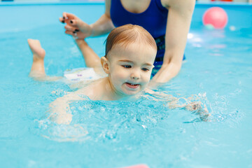 Fototapeta na wymiar A 2-year-old little boy learns to swim in a pool with a coach. Swimming lessons for children