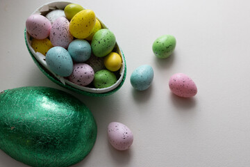A green Easter egg filled with Easter sweets in green, blue, yellow and pink. With light background