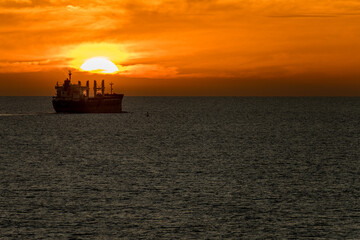 Sun setting over the water horizon with a bulk carrier cargo ship sailing away