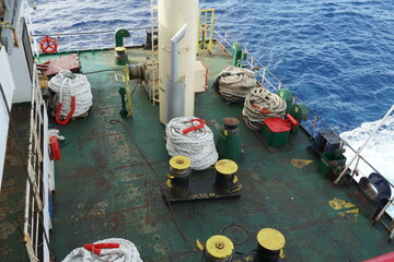 Aft mooring station situated on stern part of container ship behind superstructure. On the green painted main deck are white ropes  and black and yellow bollards and rollers with leads. 