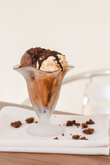 Cup of chocolate and vanilla ice cream with chocolate coating on a wooden table.