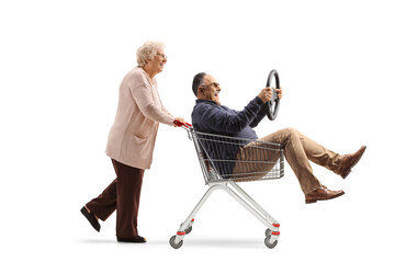 Elderly woman pushing a mature man inside a shopping cart holding a steering wheel
