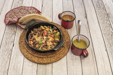 A Mexican beef wire stew cooked in a cast iron pot on cork trivets, wheat tortillas and sauces