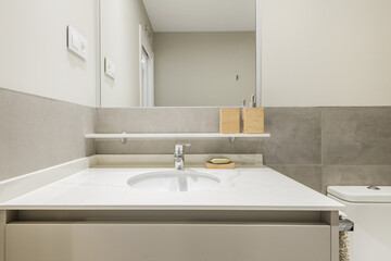 Small apartment bathroom with gray wood cabinet, frameless mirror, subtle white stone countertop, and wood bathroom fixtures