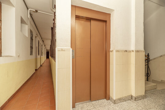 Interior Corridor Of A Building With Access Doors To Apartments, Stone Stairs And Access Doors To An Elevator In Light Brown Color