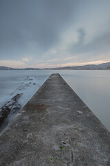 Long exposure image of a semi-abandoned stone pier at dawn next to a Galician beach