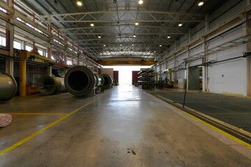 Warehouse of a factory with heavy cranes on roof rails, large mechanical parts and concrete floors