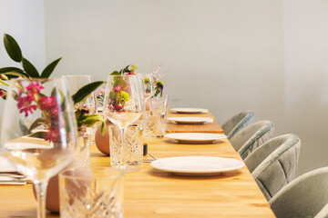 Detail of a long wooden dining table with table service with glassware, porcelain crockery and vases with flowers