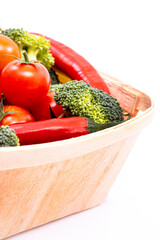 A light wooden basket filled with ripe cherry tomatoes, broccoli chunks and red hot chili pepers