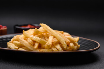 Delicious crispy french fries with salt and spices on a dark concrete background